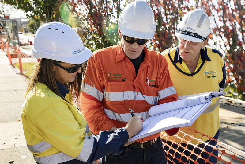 Gas industry workers in safety gear reviewing construction blueprints at a pipeline installation site.
